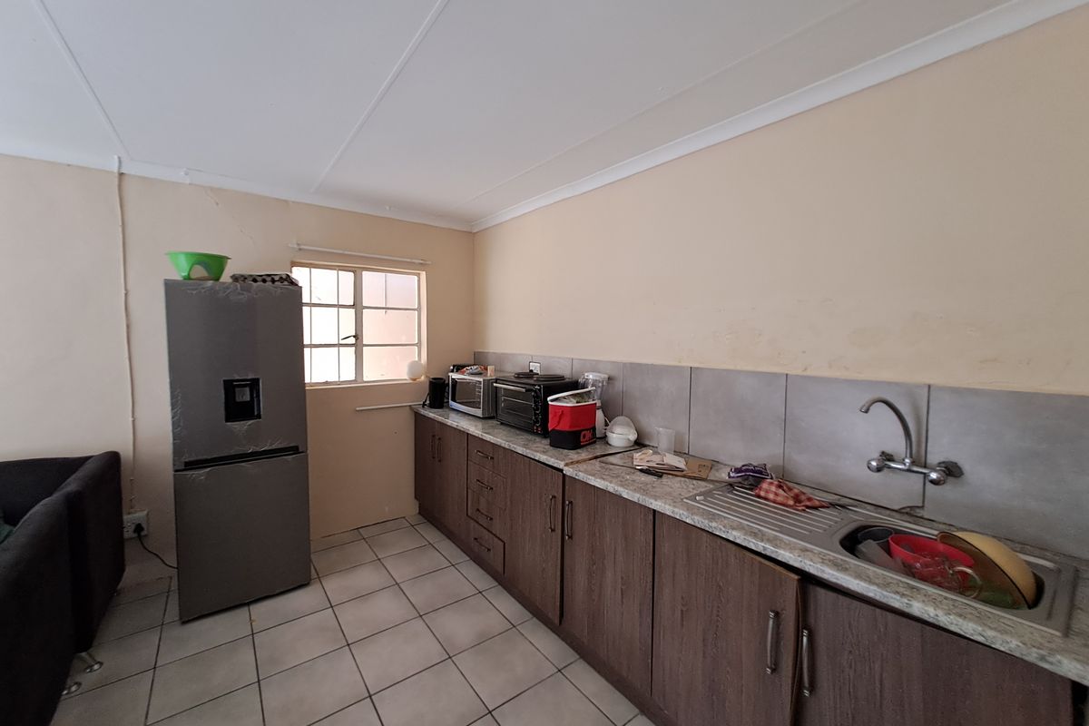 A functional kitchen featuring laminate cabinetry, stone-look countertops, a stainless steel sink, and tiled splashbacks, requiring cosmetic updates to improve its overall condition.