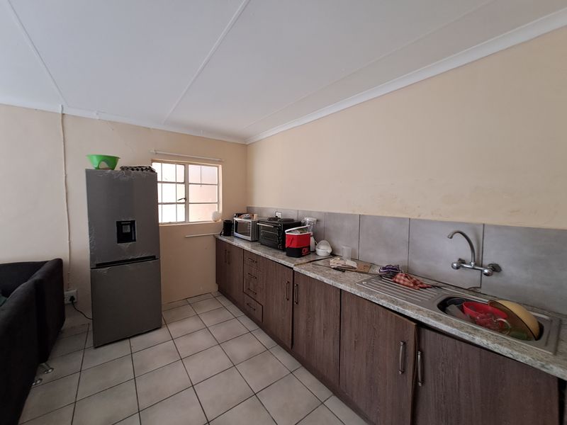 A functional kitchen featuring laminate cabinetry, stone-look countertops, a stainless steel sink, and tiled splashbacks, requiring cosmetic updates to improve its overall condition.