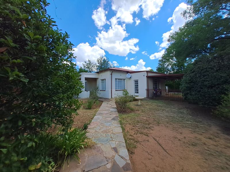 Rear view of the house featuring a stone paved walkway leading to a covered patio area set within a garden.