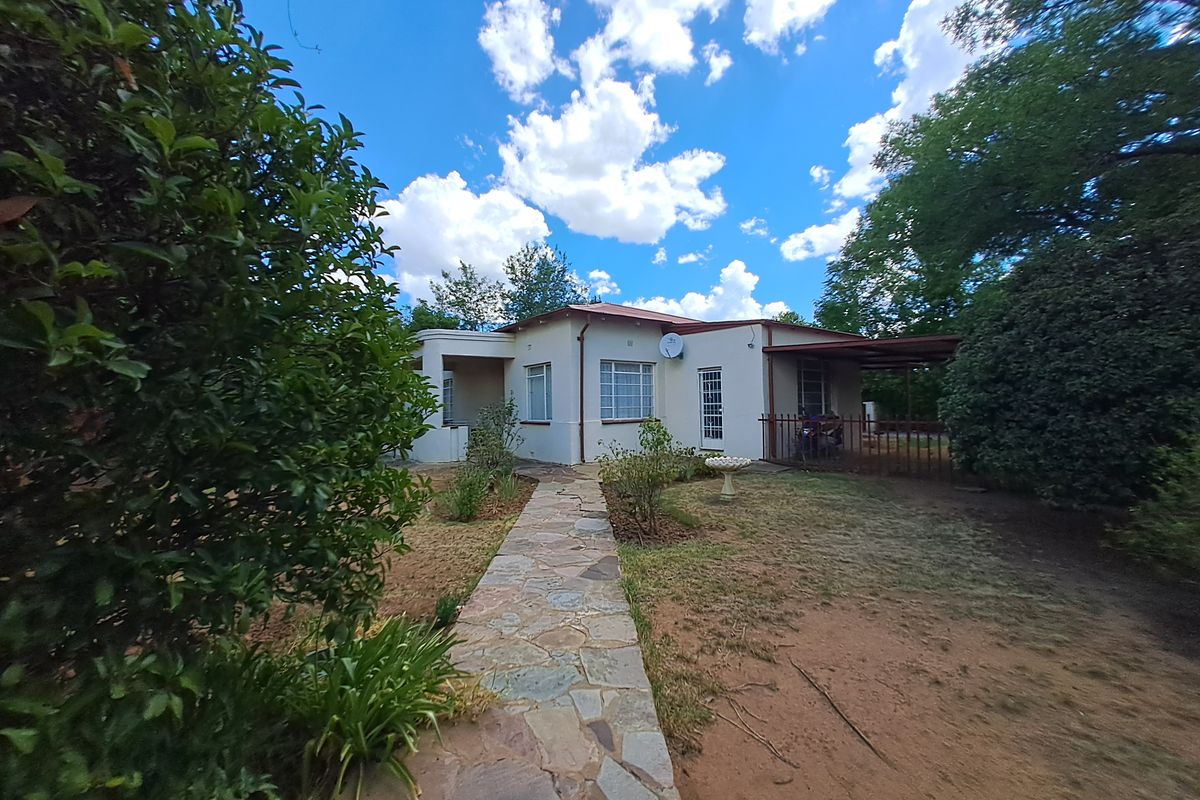 Rear view of the house featuring a stone paved walkway leading to a covered patio area set within a garden.