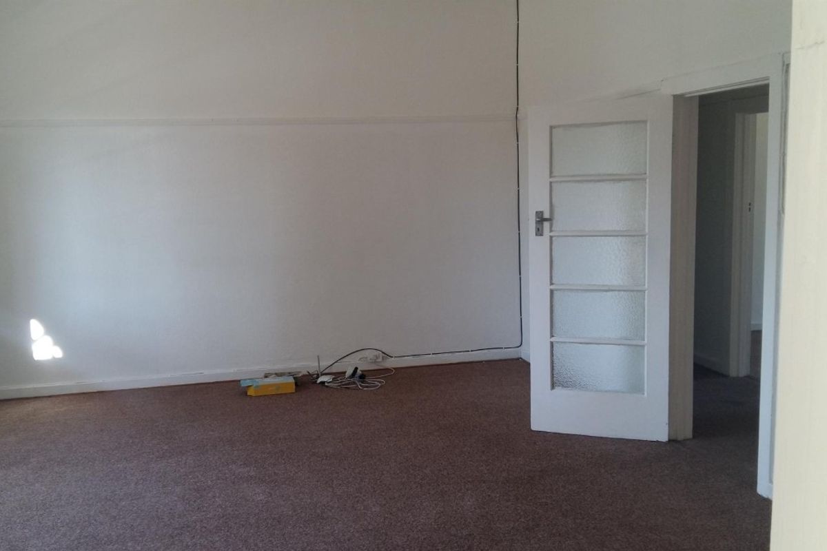An empty living room featuring brown carpet flooring and a classic multi-pane glass door, providing a blank canvas for interior design.