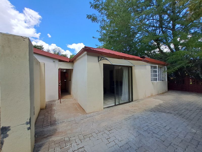 Rear exterior view of the property featuring a paved courtyard, sliding glass door access, and a metal roof structure.