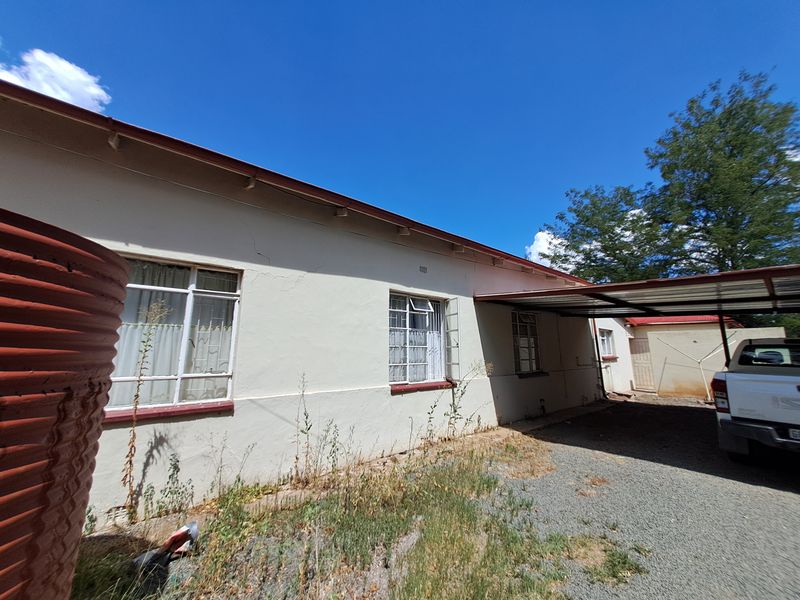Rear exterior view of the property featuring a gravel driveway, attached carport, and steel-framed windows with visible plaster cracking.