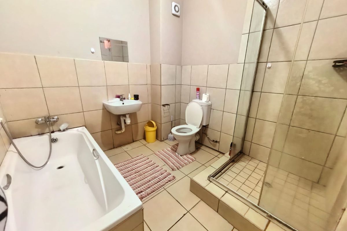 A functional bathroom featuring a bathtub, separate glass-enclosed shower, wall-mounted basin, and toilet with neutral ceramic tiling throughout.