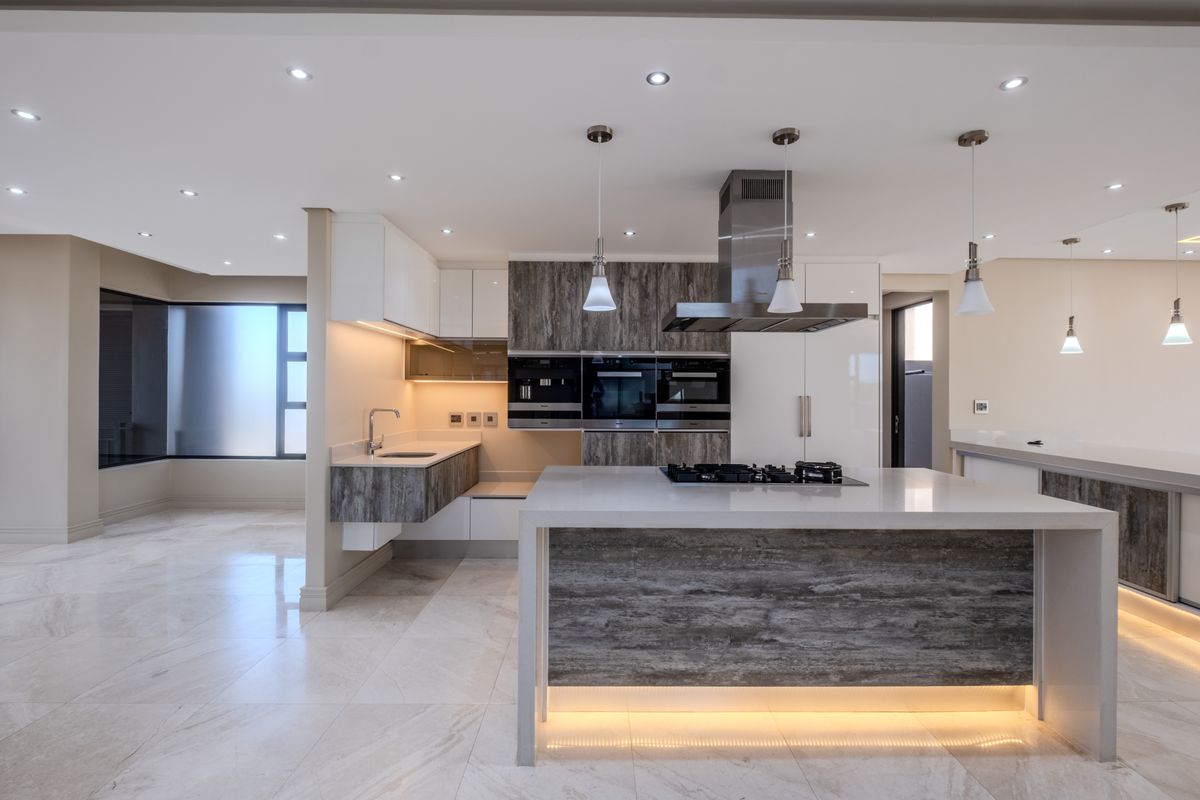 Modern, high-end kitchen featuring a large island with gas hob, integrated appliances, stone countertops, and sophisticated recessed and under-cabinet lighting.