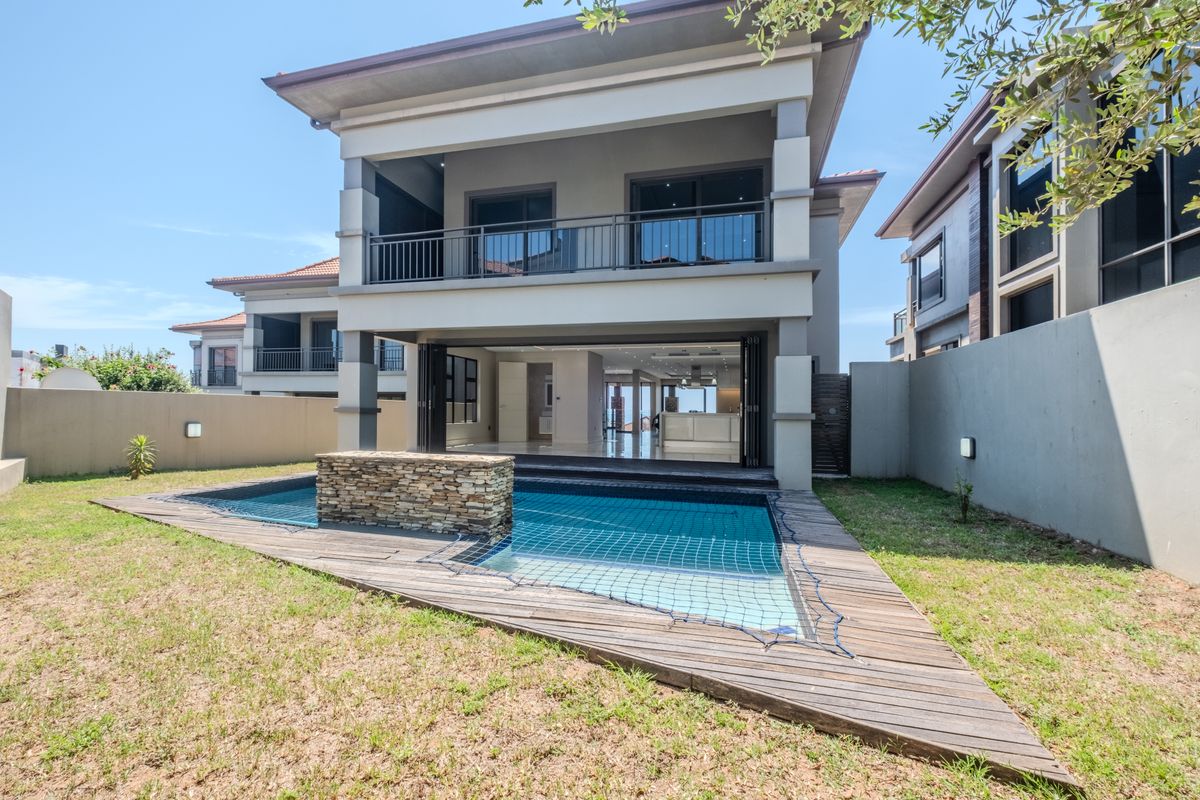 Rear view of a modern townhouse featuring a swimming pool with a stone water feature, timber decking, and a spacious balcony.