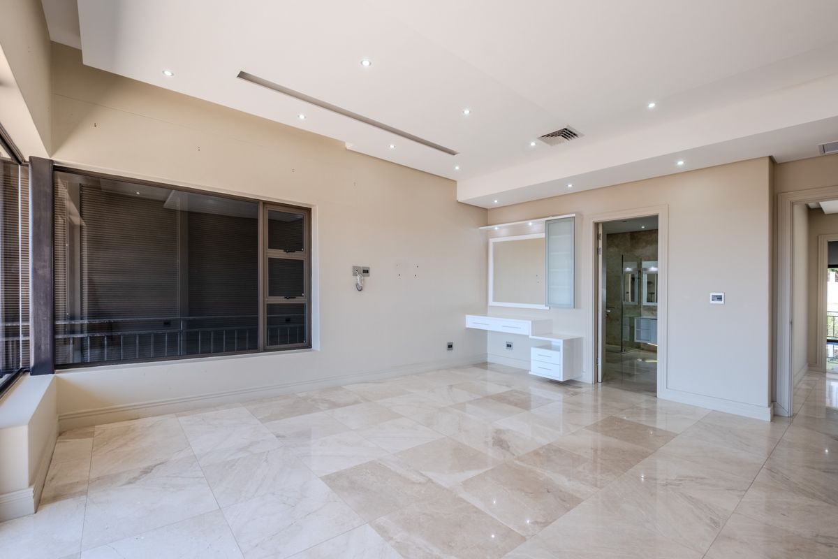 Spacious bedroom featuring polished marble flooring, recessed ceiling lighting, ducted air conditioning, and a built-in vanity unit with direct access to an en-suite bathroom.
