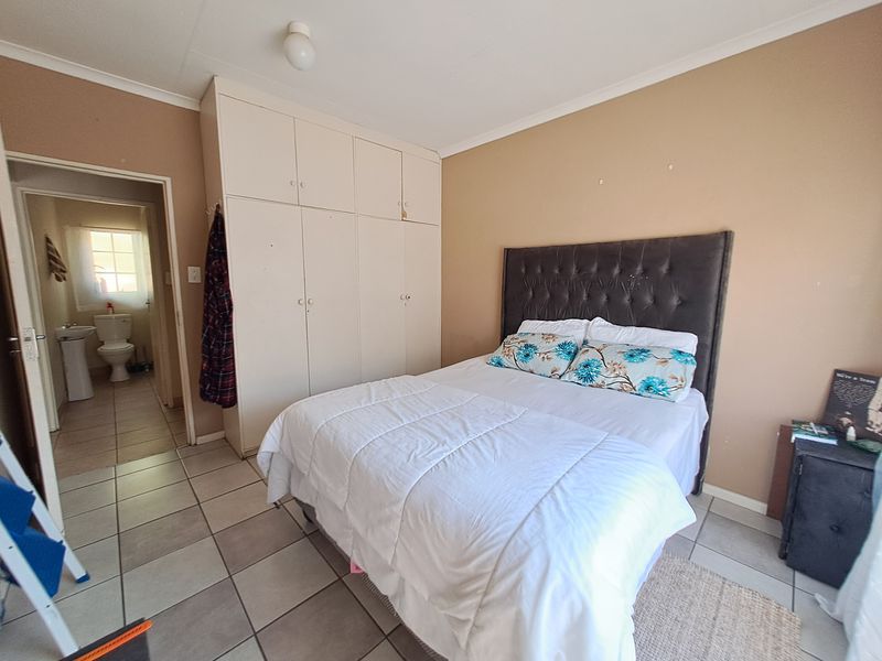 A bedroom featuring tiled flooring and built-in cupboards, with an adjoining bathroom visible through the doorway.