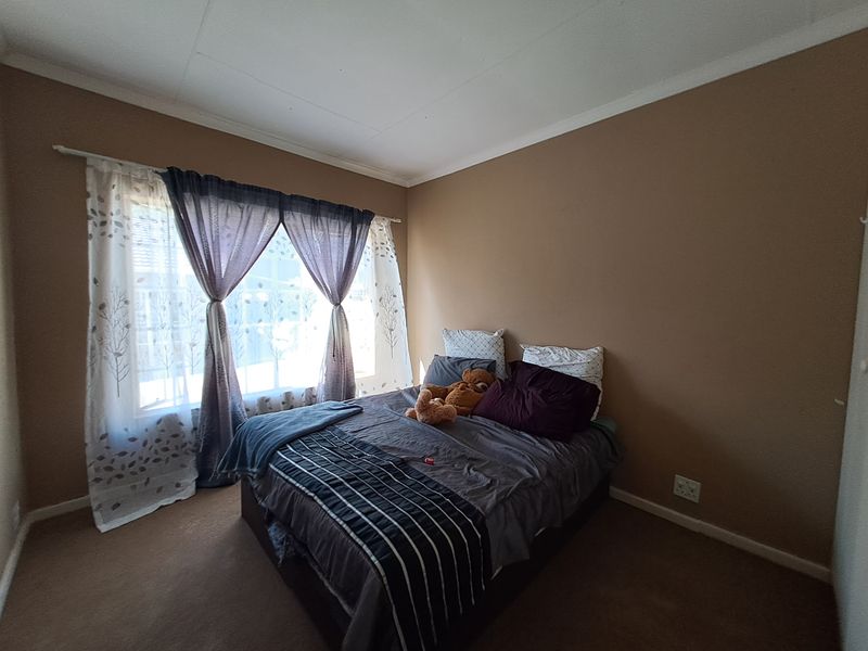 A standard bedroom featuring carpeted flooring and a window with a curtain rod, providing a neutral space ready for personalization.