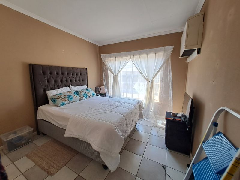 A bedroom featuring tiled flooring, an installed air conditioning unit, and neutral wall tones, offering a functional space ready for cosmetic updates.