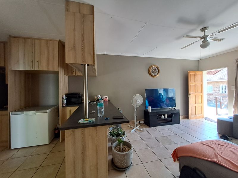 Open-plan living and kitchen area featuring light wood cabinetry, a breakfast bar, tiled flooring, and direct access to the exterior.