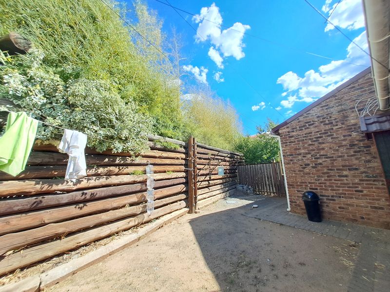 A rear exterior view of the property featuring a brick wall, a log fence boundary, and a paved walkway area.