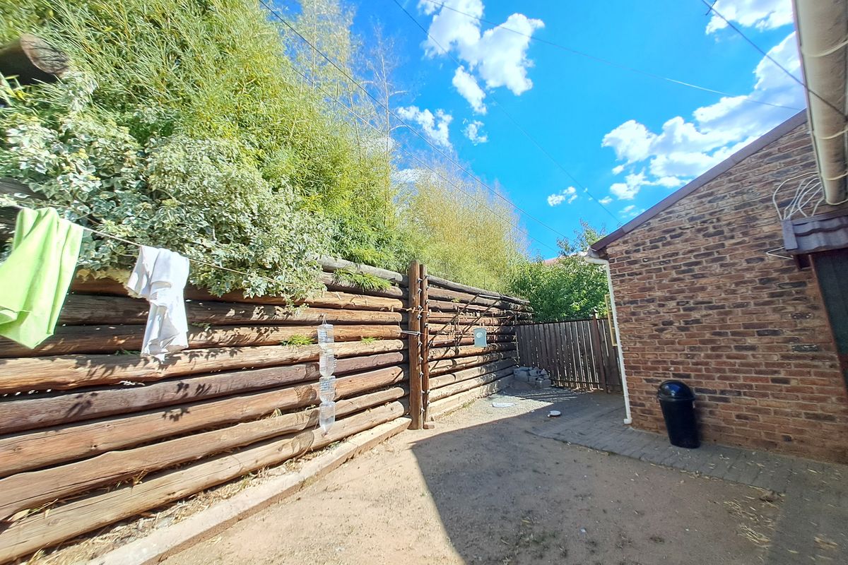 A rear exterior view of the property featuring a brick wall, a log fence boundary, and a paved walkway area.