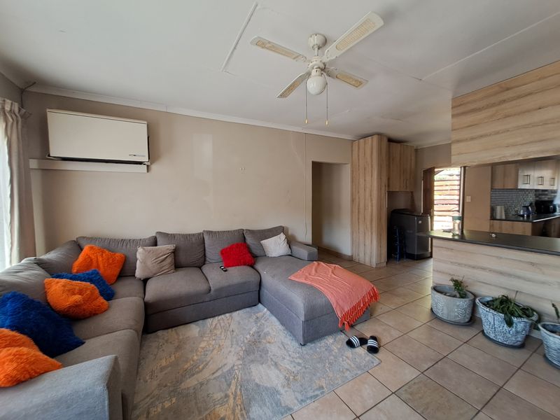 Open-plan living area featuring tiled floors, a ceiling fan, air conditioning, and a functional kitchen with built-in cabinetry and a breakfast bar.