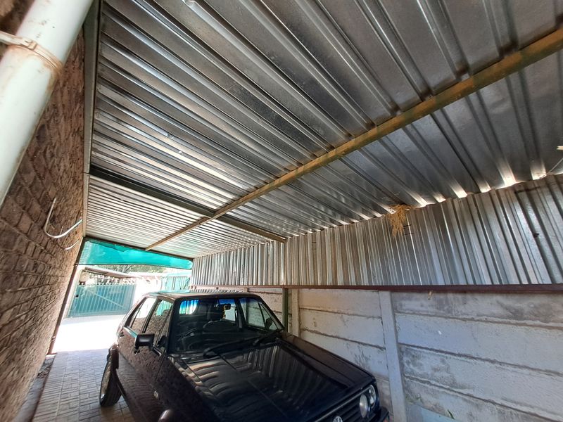 A covered parking area featuring a corrugated metal roof structure and precast concrete walling with paved flooring.