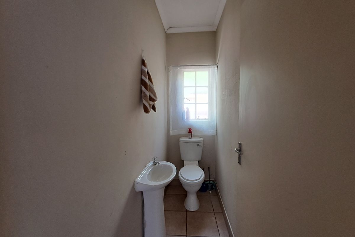 A compact guest bathroom featuring a pedestal basin, toilet, and tiled flooring with natural light from a small window.