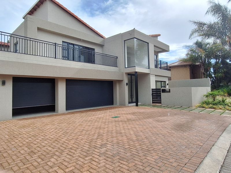 Modern double-story residential property featuring a paved driveway, double garage, and an upper-level balcony with metal railings.
