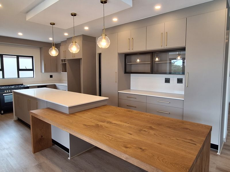 Modern, spacious kitchen featuring sleek cabinetry, a large island with a wooden breakfast bar, quartz countertops, and high-end built-in appliances.