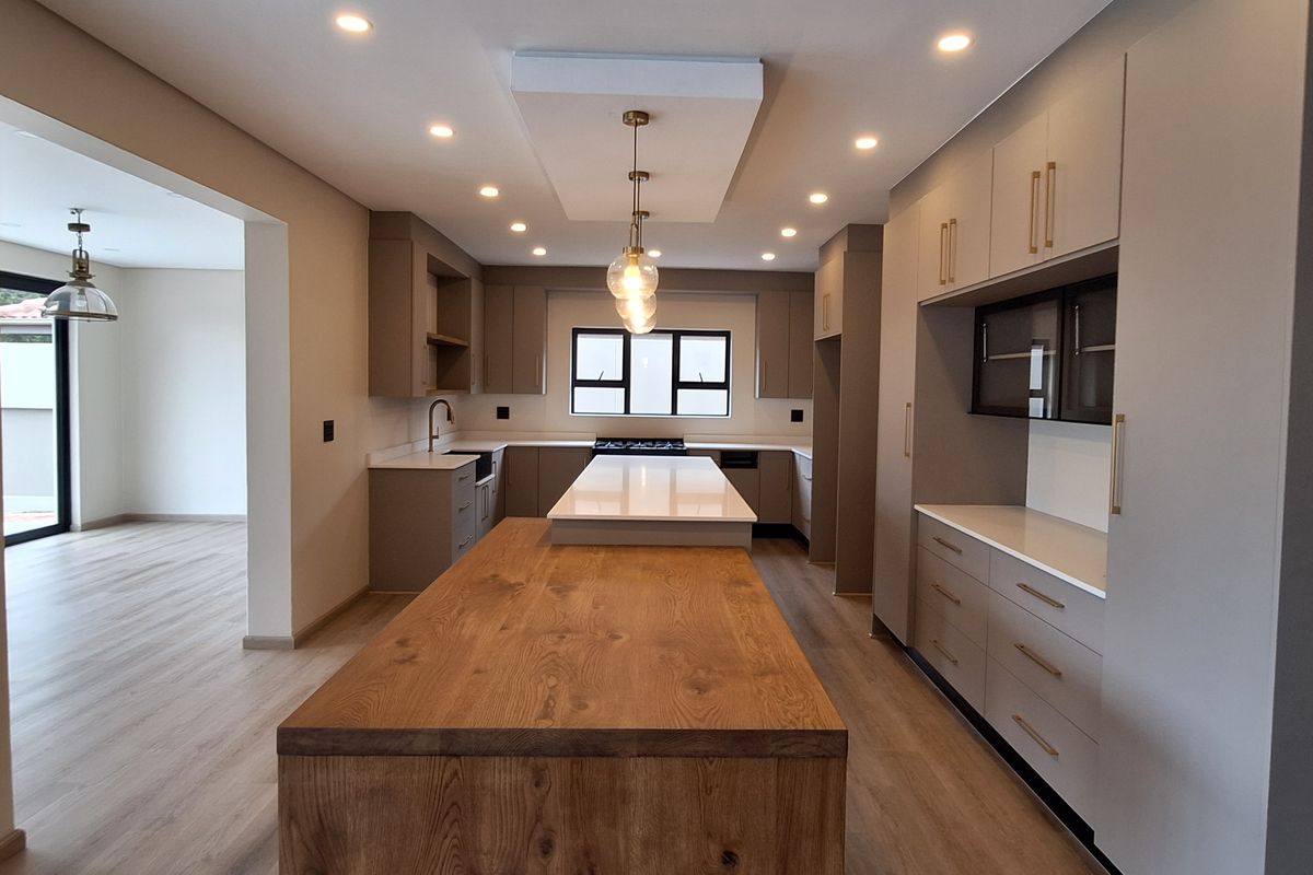 Modern kitchen featuring a large central island with a wooden breakfast bar, stone countertops, ample built-in cabinetry, and recessed lighting.