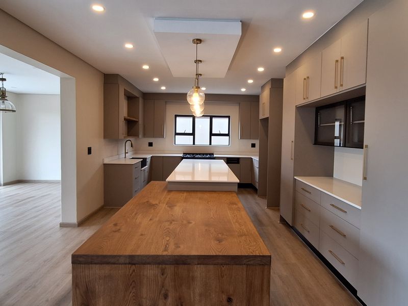 Modern kitchen featuring a large central island with a wooden breakfast bar, stone countertops, ample built-in cabinetry, and recessed lighting.