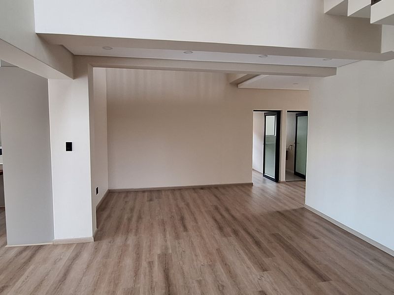 Spacious open-plan living area featuring modern laminate flooring, recessed lighting, and a sleek kitchen with a built-in island and staircase access.