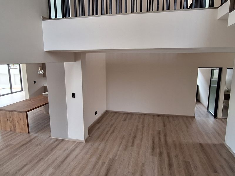 Spacious open-plan living area featuring modern laminate flooring, a double-volume ceiling, and a contemporary staircase with a sleek metal balustrade.