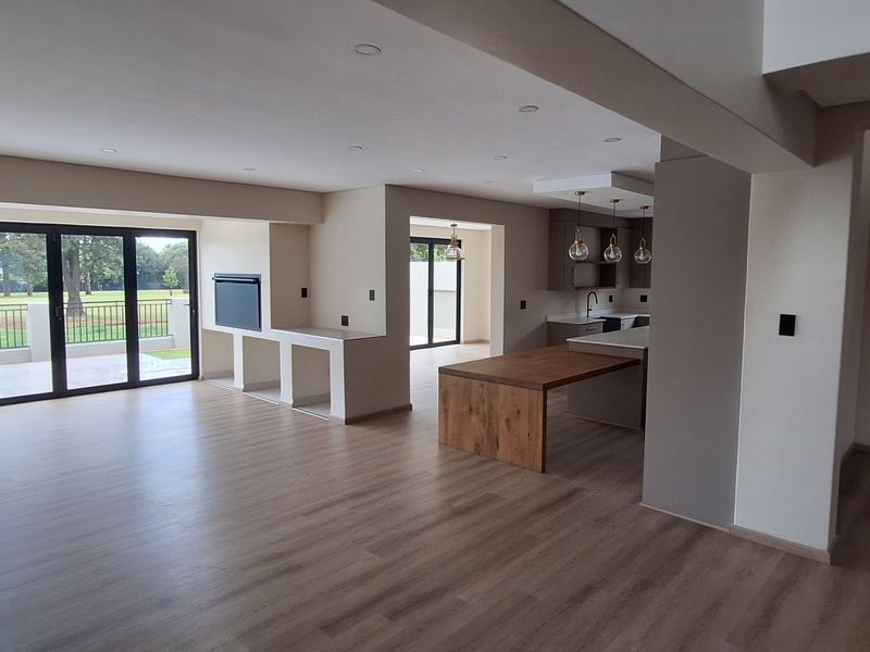 Spacious open-plan living and kitchen area featuring modern laminate flooring, recessed lighting, a built-in fireplace, and large bi-fold doors leading to the exterior.