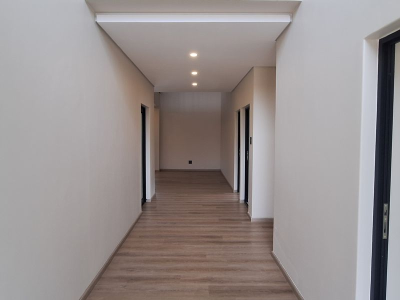 A clean, modern hallway featuring neutral walls, recessed downlighting, and wood-look laminate flooring, providing access to multiple rooms.