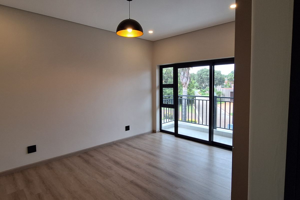 A bright, empty bedroom featuring modern laminate flooring, recessed lighting, and a sliding glass door leading to a private balcony.