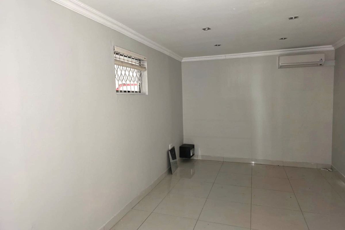 A bright, empty living room featuring neutral tiled flooring, recessed ceiling lighting, crown molding, and a wall-mounted air conditioning unit.