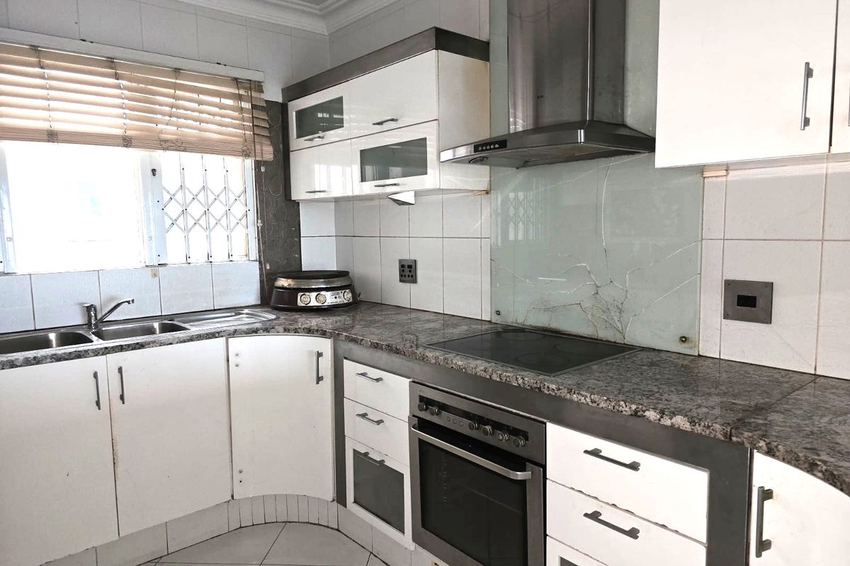 Functional kitchen featuring granite countertops, built-in oven, electric hob, stainless steel extractor fan, and ample white cabinetry with a tiled splashback.