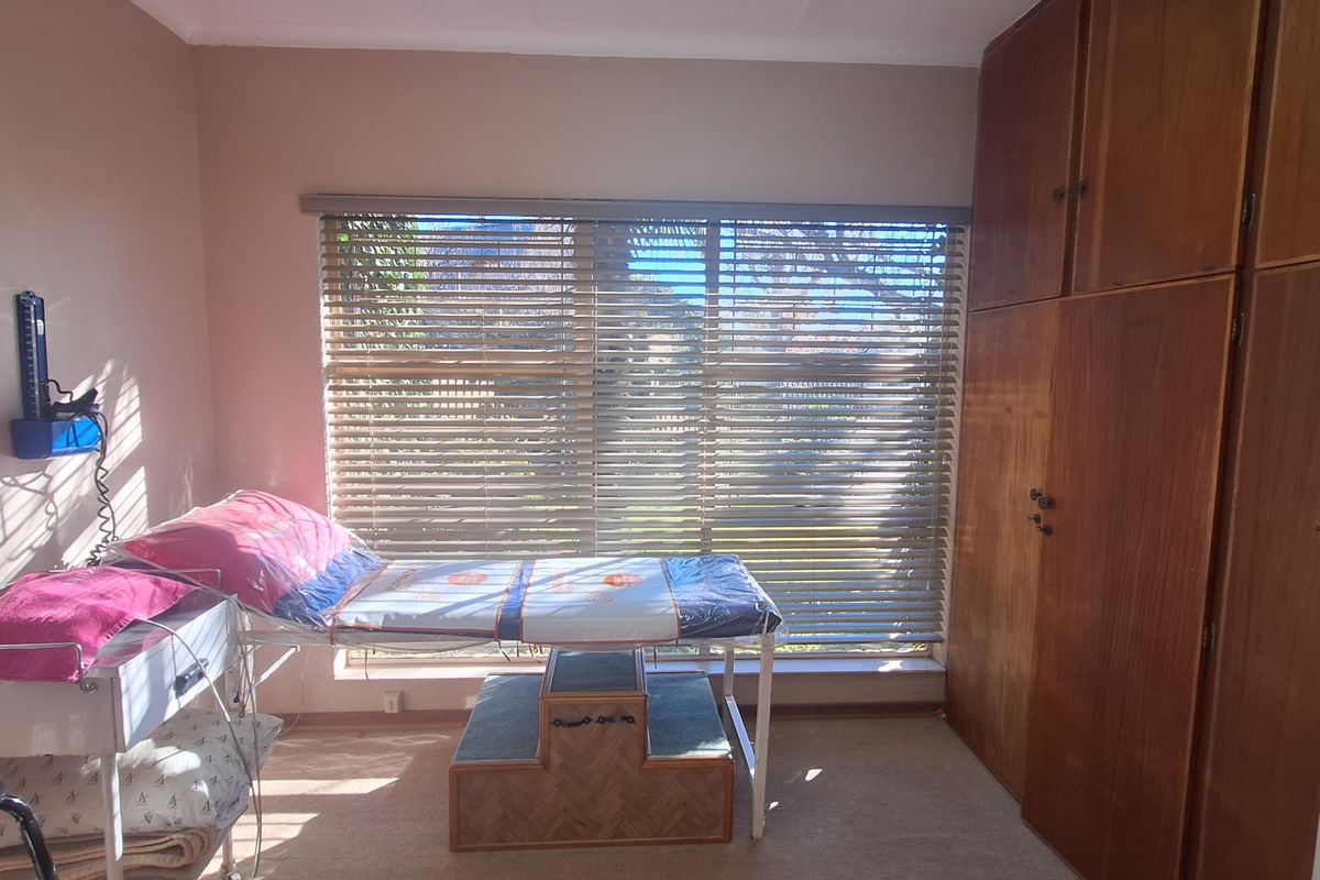 A bedroom featuring built-in wooden cupboards and carpeted flooring, currently utilized as a clinical or treatment space with natural light through window blinds.