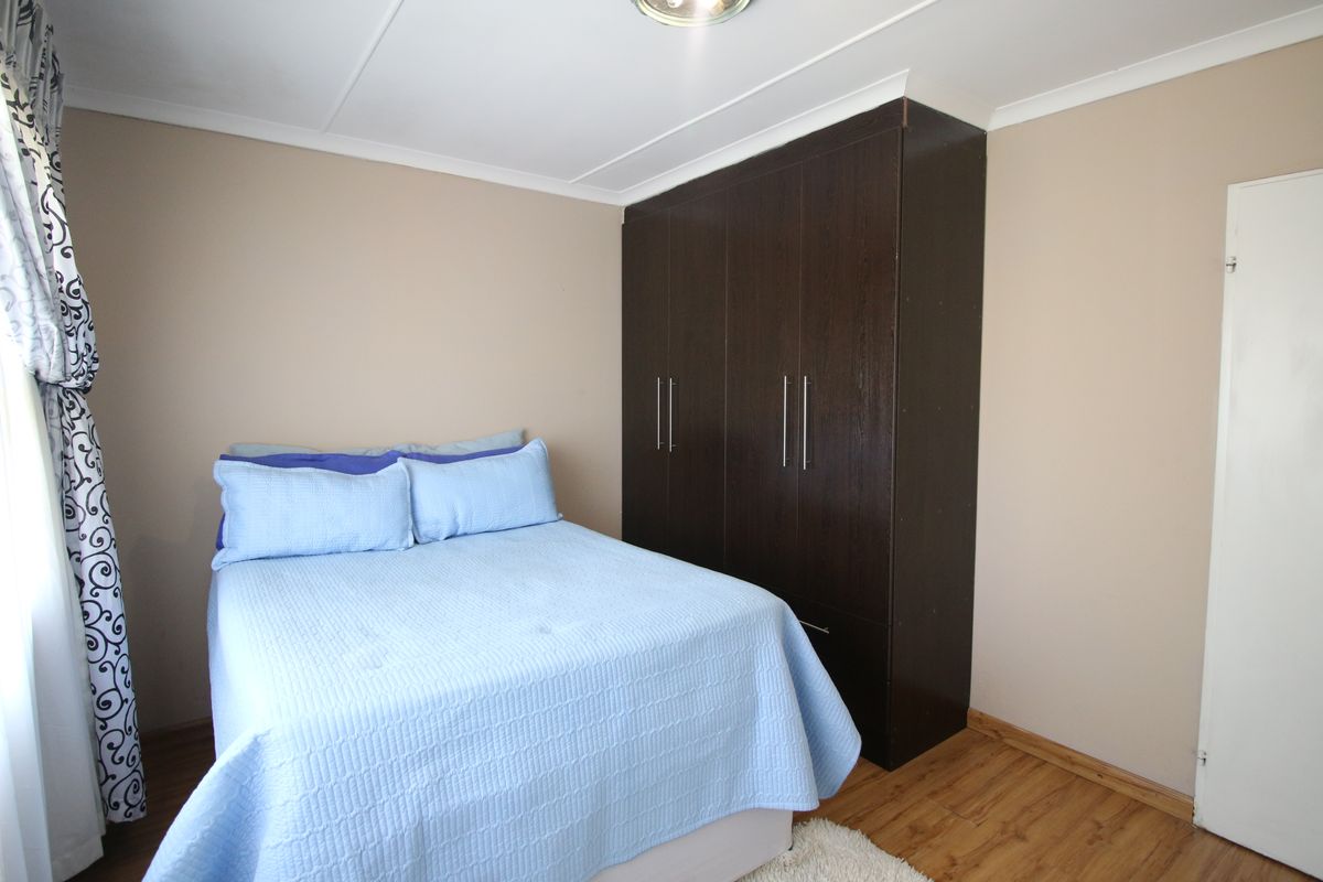 A bedroom featuring laminate flooring and a dark wood built-in wardrobe with modern handles.