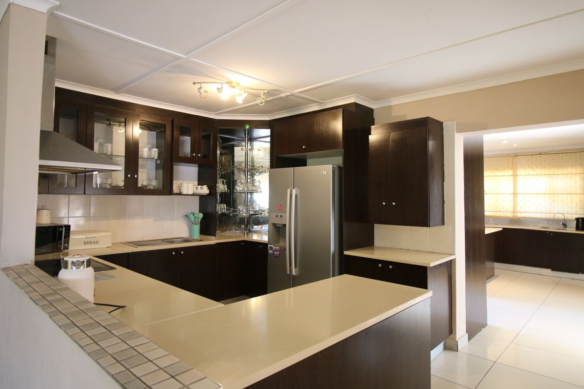 A functional kitchen featuring dark wood cabinetry, stone countertops, a stainless steel extractor fan, and a tiled backsplash, with an adjacent scullery area.