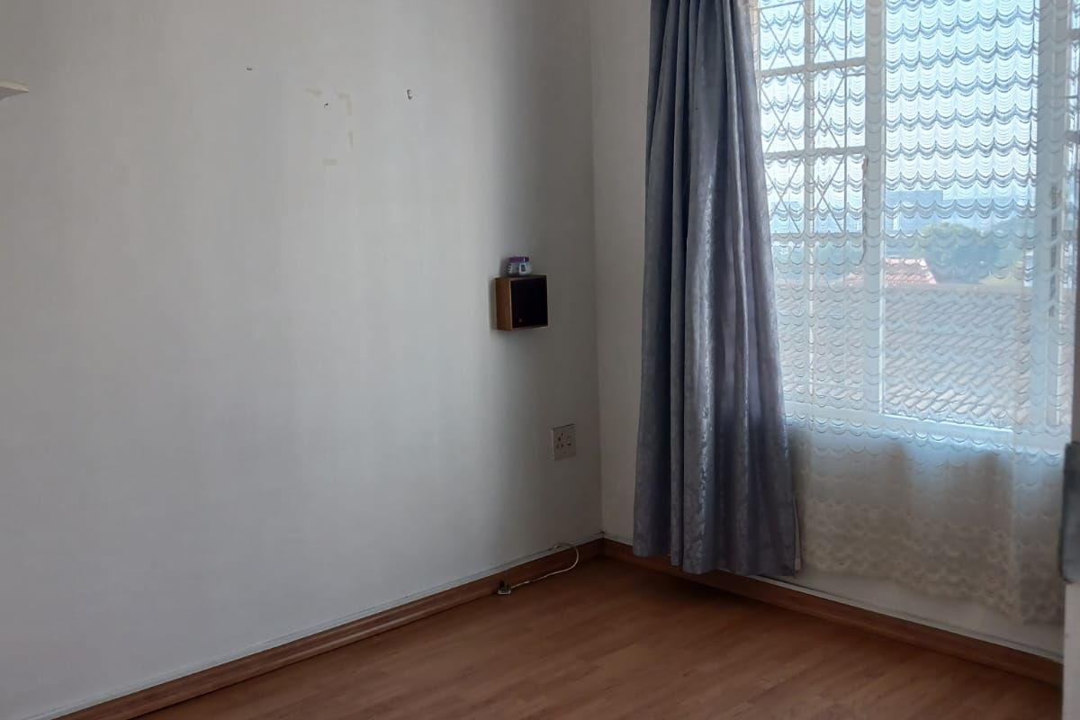 An empty bedroom featuring laminate flooring, a window with security bars, and neutral wall finishes, ready for personalization.