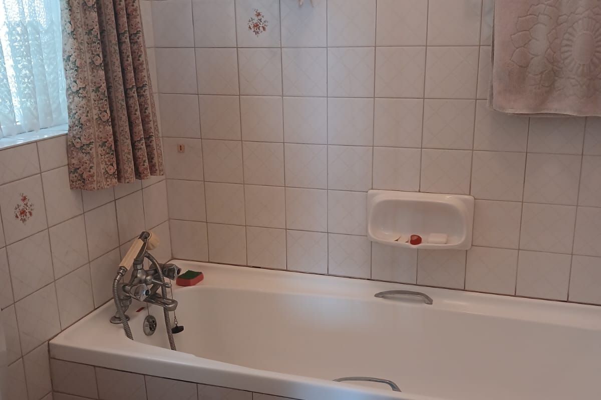 A dated bathroom featuring a standard bathtub with wall-mounted fixtures, tiled walls, and a toilet. The space requires cosmetic updates and repairs.