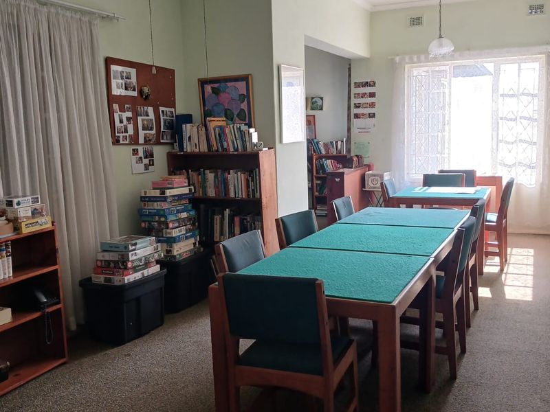 Spacious dining area featuring neutral walls, carpeted flooring, and large windows with security gates, providing a functional space for gatherings.