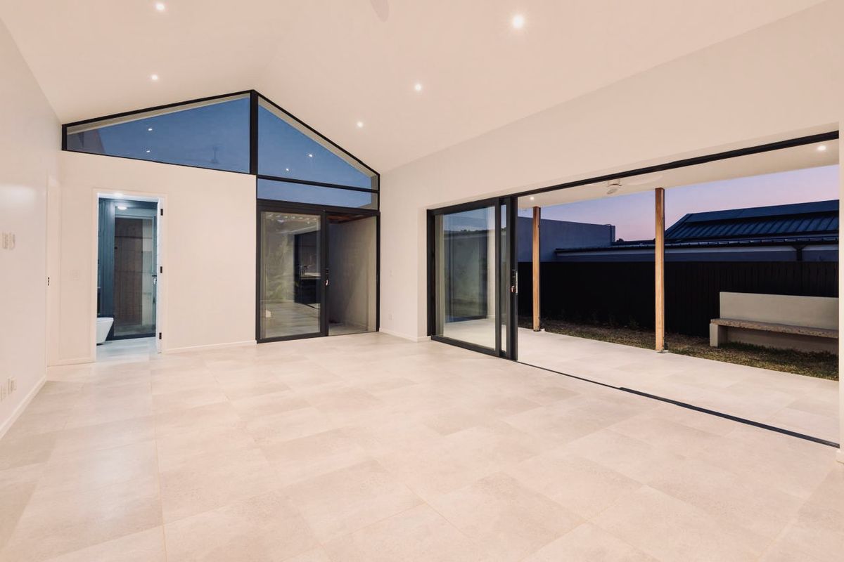 Spacious, light-filled living area featuring vaulted ceilings, large format floor tiles, and seamless indoor-outdoor flow through expansive sliding glass doors to a covered patio.