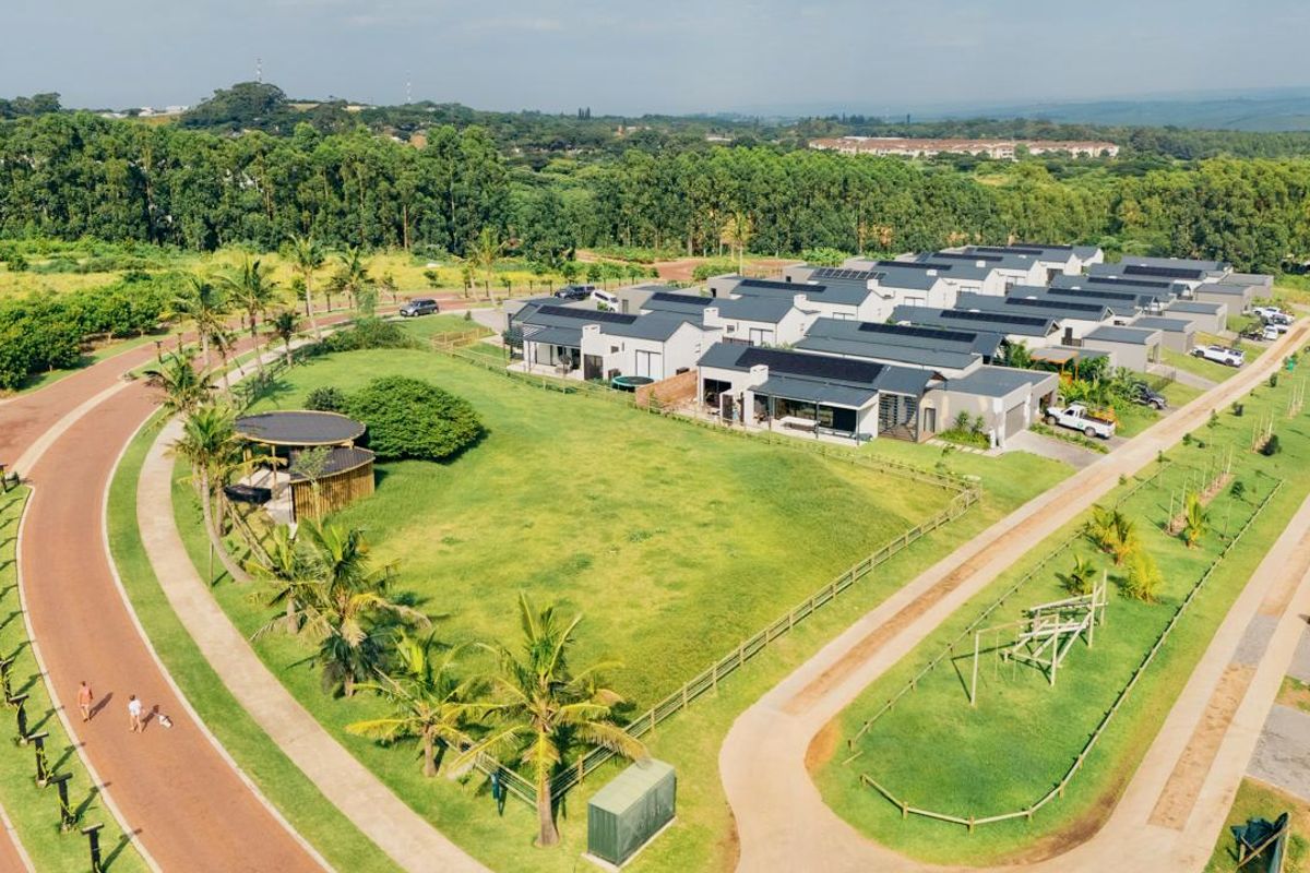Aerial view of a modern residential estate featuring multiple homes with solar panels, landscaped green spaces, and paved access roads.