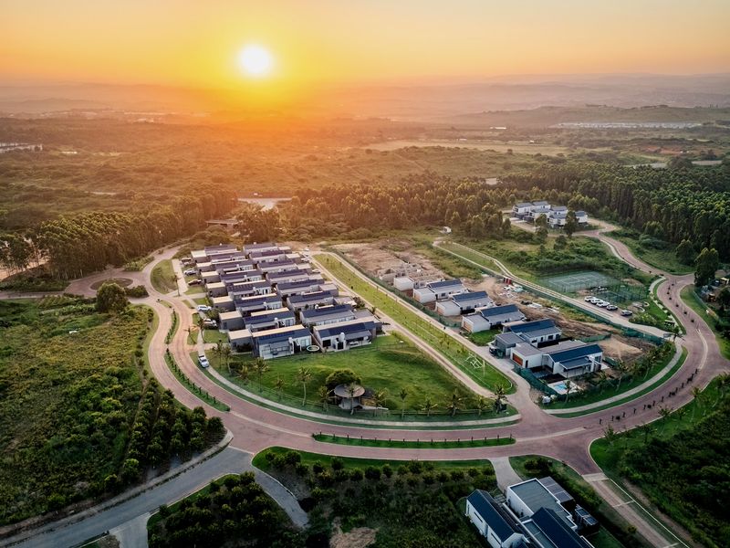 Aerial view of a modern residential estate at sunset, featuring paved roads, landscaped surroundings, and communal recreational facilities.