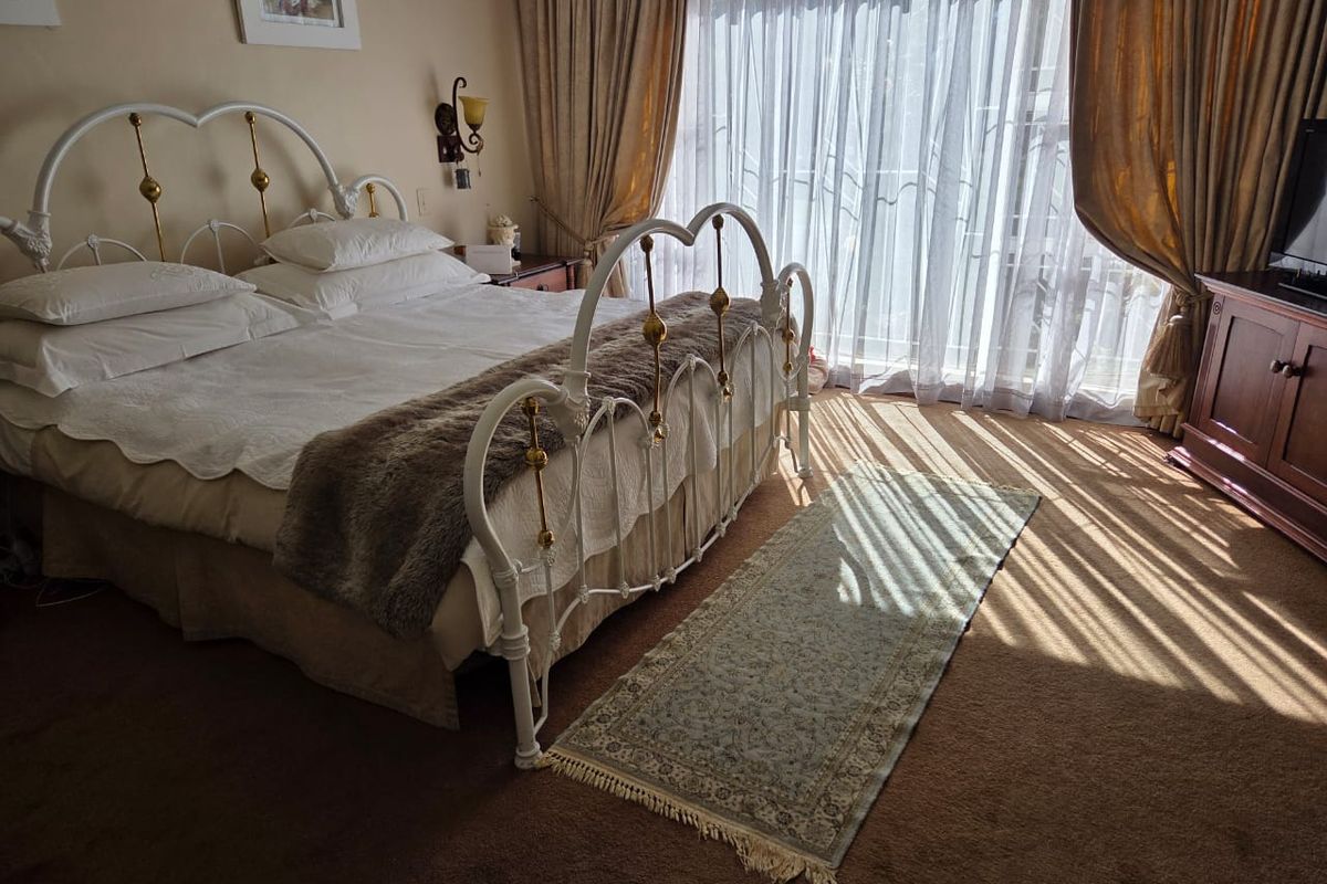 A well-lit bedroom featuring carpeted flooring, large sliding glass doors with curtains, and wall-mounted lighting fixtures.