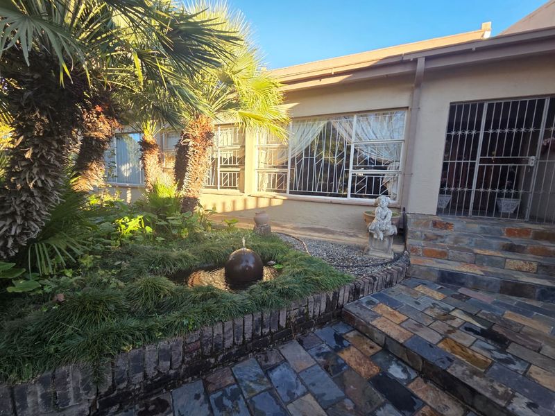 A rear garden area featuring a stone-paved patio, a small water feature, mature palm trees, and security bars on the windows and doors.
