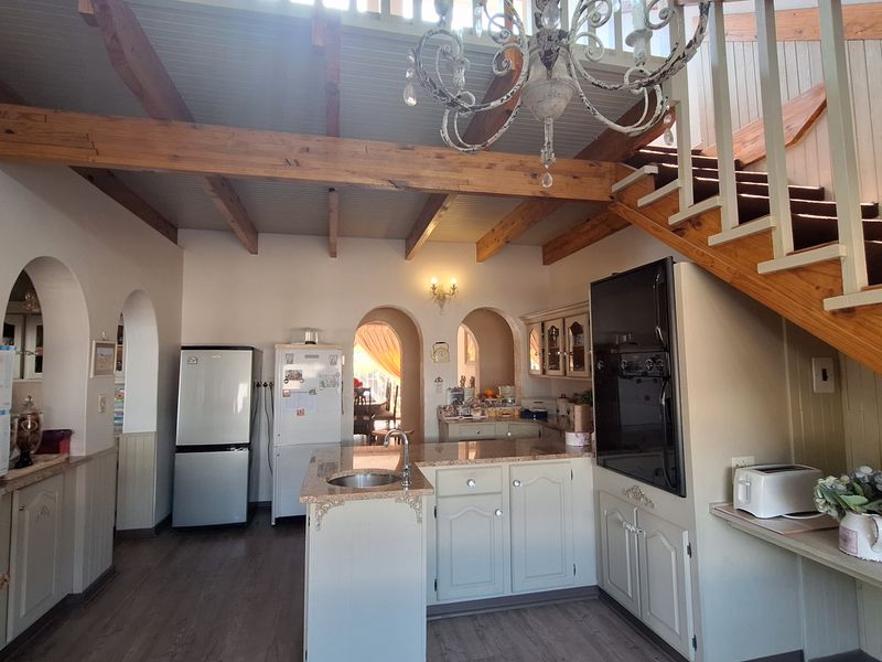 Open-plan kitchen featuring a central island with sink, built-in oven, timber ceiling beams, and a staircase leading to an upper mezzanine level.