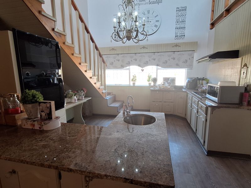 Open-plan kitchen featuring granite countertops, a central island with a prep sink, built-in oven, and a staircase leading to a mezzanine level.