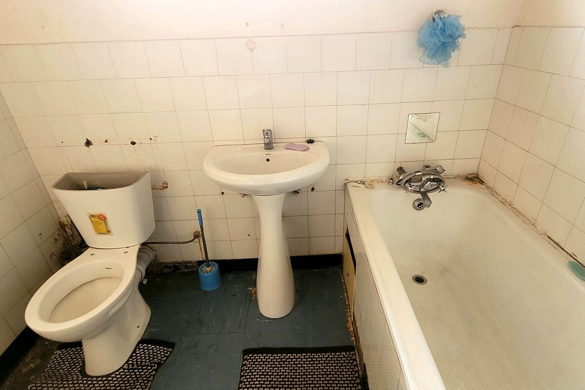 A dated bathroom featuring a pedestal basin, toilet, and bathtub with tiled walls, requiring significant renovation and cosmetic updates to improve its condition.