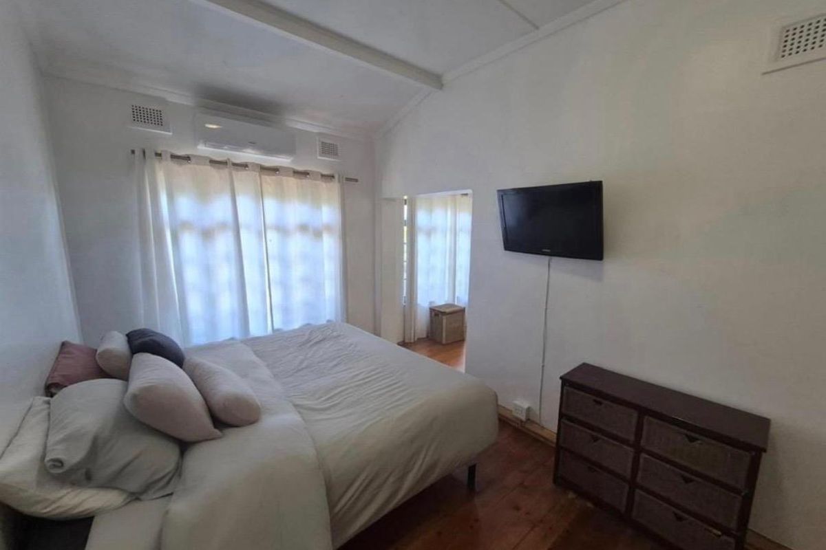 A bedroom featuring timber flooring, a wall-mounted television, and a split-system air conditioning unit.