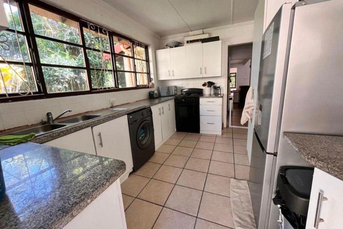 Functional kitchen featuring granite countertops, double basin sink, tiled flooring, and ample built-in cabinetry with views to the garden.