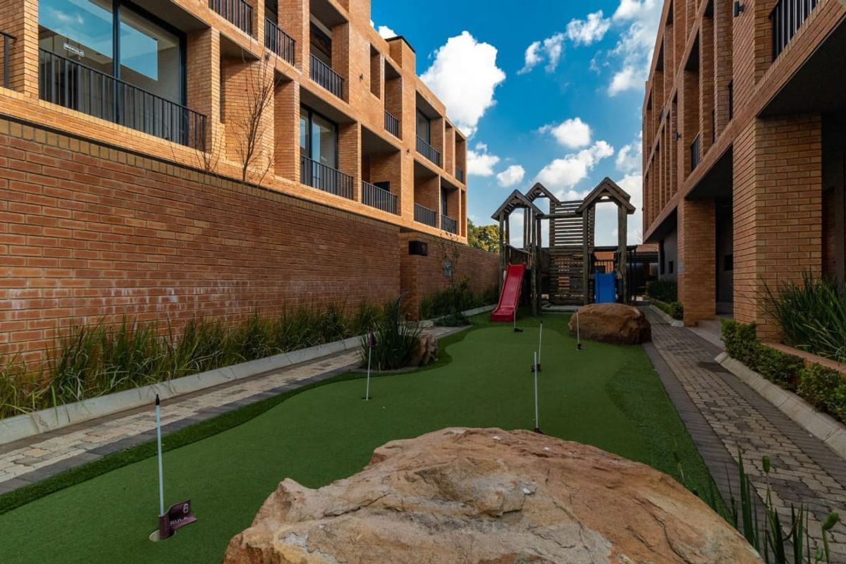 A well-maintained communal outdoor area featuring a mini-golf course, playground equipment, and brick apartment building facades with balconies.