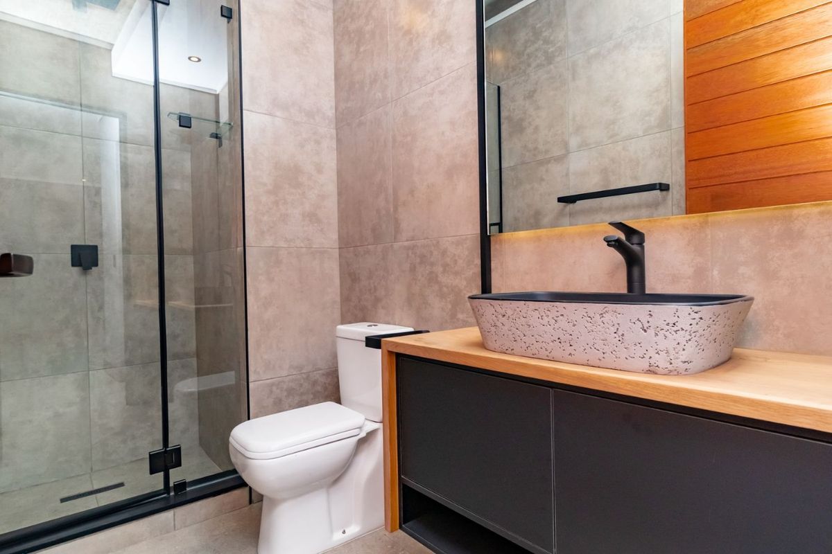 Modern bathroom featuring a glass shower enclosure, vessel sink on a vanity cabinet, and contemporary black fixtures with neutral wall tiling.
