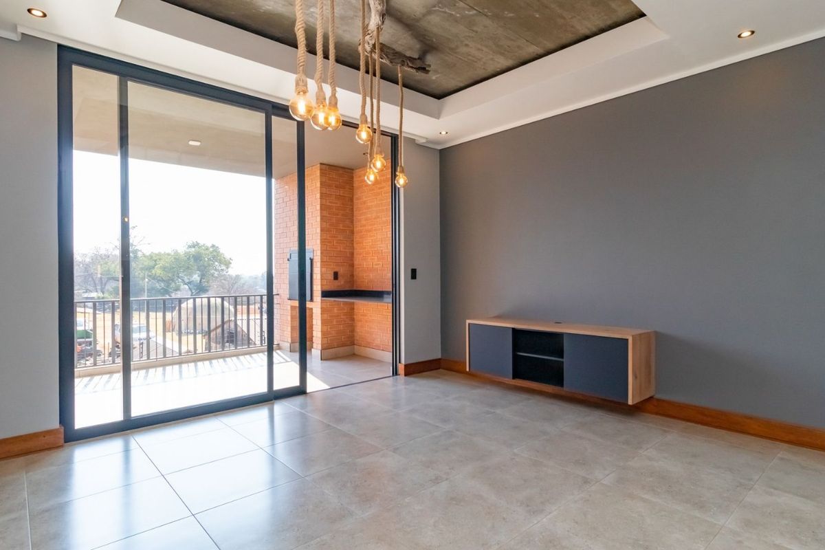 Modern living area featuring tiled floors, a unique exposed concrete recessed ceiling, and large sliding doors opening to a private balcony with a built-in braai.